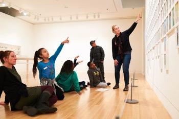 在画廊里，学生们和老师一起指着一幅艺术作品